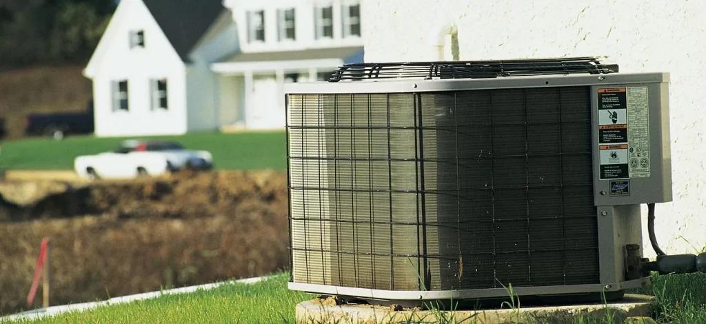 outer unit of hvac system is in picture and a house in background.